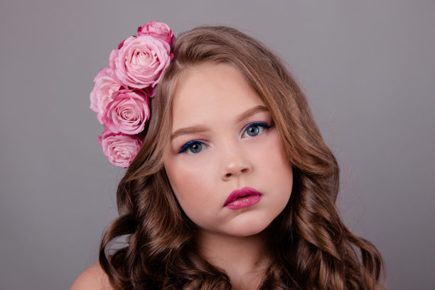 一个漂亮的黑发女孩的肖像，她的头发上有粉红色的玫瑰在灰色的背景。头上卷着的花。春天,花,颜色。时尚的照片图片下载