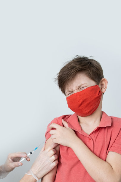 2019冠状病毒病大流行期间，一名戴着医用口罩的儿童接种了抗冠状病毒疫苗。医生在医疗手套与注射器进行注射。本空间图片下载