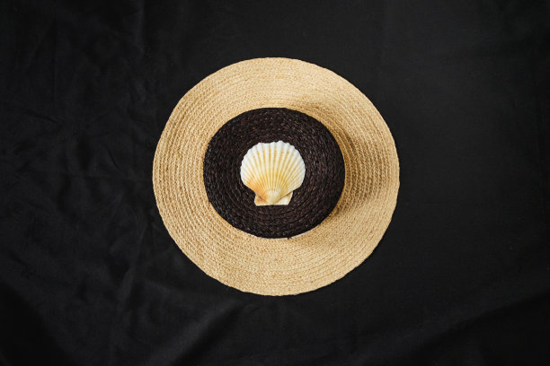 黑布上放着一顶顶上有贝壳的草帽。图片下载