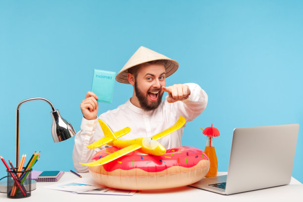 快乐轻松的胡子男戴着滑稽的帽子指着拿着护照的你，推荐热门的出国旅游，救生圈和躺在工作场所的玩具飞机图片下载