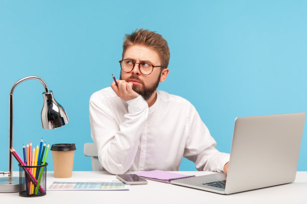 有思想的大胡子记者在工作场所用笔记本电脑写文章，在笔记本上记笔记，思考标题图片下载