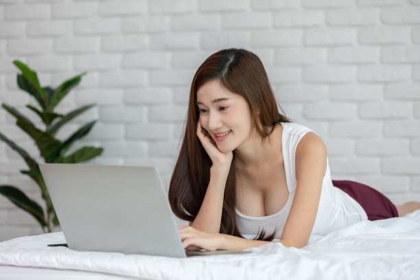 美丽迷人的亚洲年轻女子躺在床上，使用笔记本电脑使用社交媒体和网上购物放松在舒适的卧室在假期，生活方式在家里的概念图片下载