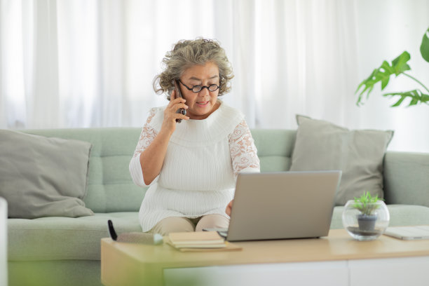 一名白发苍苍的亚洲老年妇女通过手机与客服沟通，以寻求解决电脑问题或人为失误的解决方案素材图片