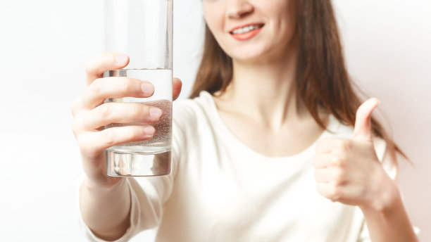 健康的生活方式。白种女性手持一杯清水给镜头微笑，选择性近距离聚焦。医疗保健。健康饮食的概念。景深浅图片下载