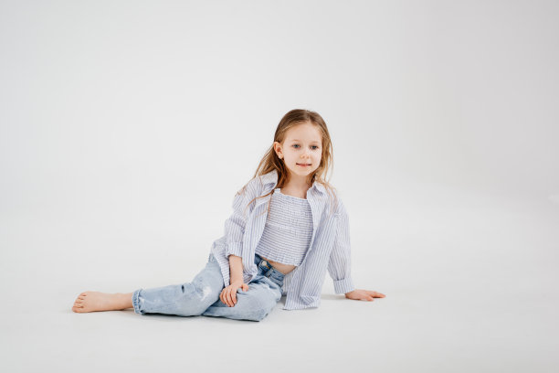 穿着牛仔裤和衬衫的长发小女孩在白色背景下摆姿势。图片下载