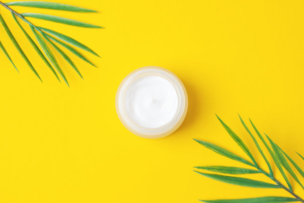 黄色背景上带有棕榈叶的化妆膏。平铺，拷贝空间图片下载