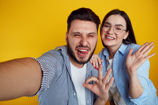 情侣们在手机上自拍，在黄色背景上做手势图片下载