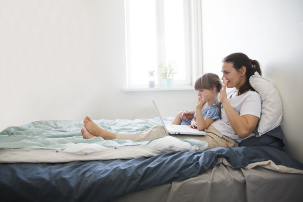 快乐的家庭，妈妈和孩子挥手打招呼，看着摄像机，问候远方的朋友，坐在床上用笔记本电脑。图片下载