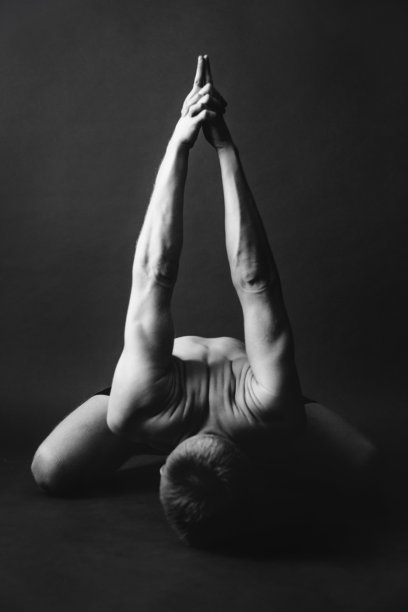 瑜伽锻炼。男子在黑暗的背景下做瑜伽体式。时尚的运动摄影工作室。黑与白，暗与模糊摄影图片下载