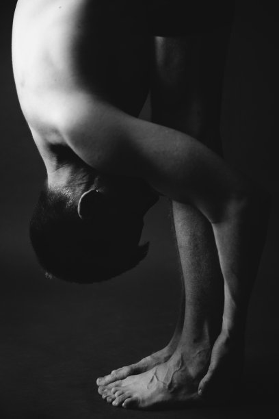 瑜伽锻炼。男子在黑暗的背景下做瑜伽体式。时尚的运动摄影工作室。黑与白，暗与模糊摄影图片下载