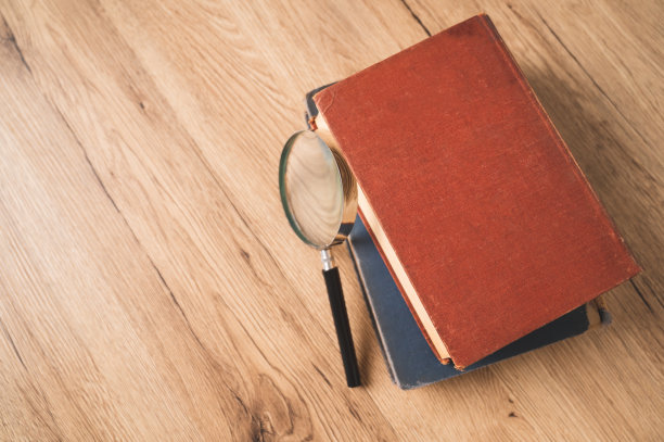 俯视图放大镜放在一堆书的木桌上，进行概念研究、搜寻和阅读。图片下载