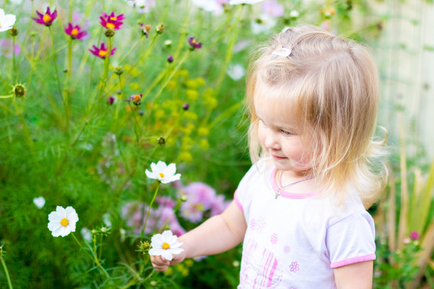 婴儿站在鲜花盛开的草地上，周围都是夏天的鲜花。明亮的夏天的照片;图片下载