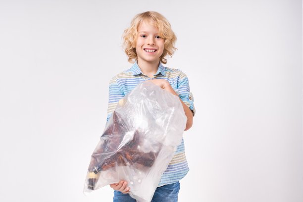 快乐的白人学校男孩拿着塑料袋的瓶子为回收孤立的白色图片下载