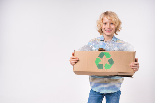 一个环保的白人男孩拿着一个装满塑料瓶的盒子供回收利用，孤立在白色背景上图片下载