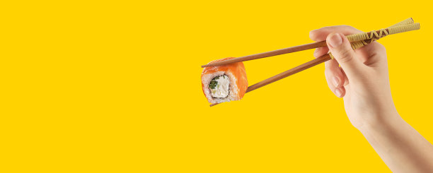 女人的手拿着寿司卷。黄色背景。创造性的概念图片下载