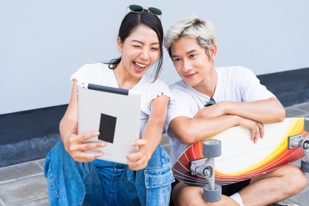 亚洲可爱的女人坐在滑板上，英俊的男人坐在街道周围的滑板道，而他们是快乐的自拍在凉爽的墙前，在白天，暑假图片下载