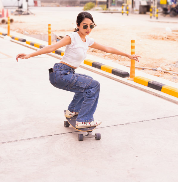 亚洲可爱的女孩或女人冲浪滑板和缩写她的身体街头在白天，暑假滑板道图片下载