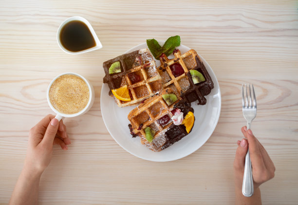 美味的早餐食品。拿着一杯咖啡，吃着加水果和糖浆的比利时华夫饼图片下载