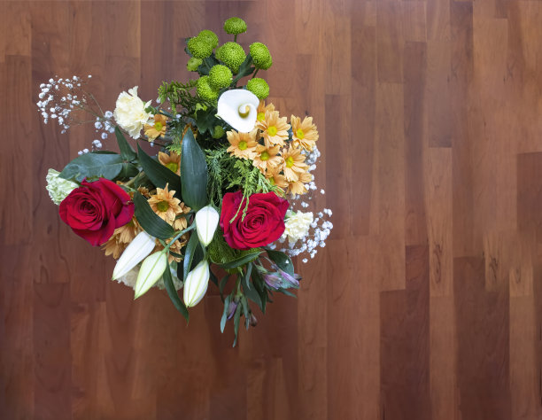 俯视图花束上有玫瑰、马蹄莲、雏菊和康乃馨，放在木地板上，选择性的集中在花束上，复制空间图片下载