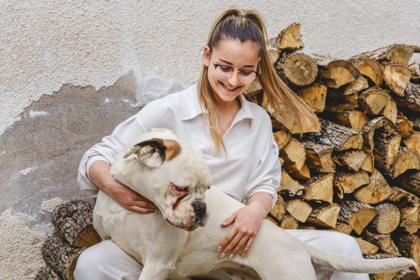 年轻的白人妇女坐在楼梯在她的家在白天与白色的狗玩他和照顾-友谊和宠物爱的概念真实的人明亮的照片前视图图片下载