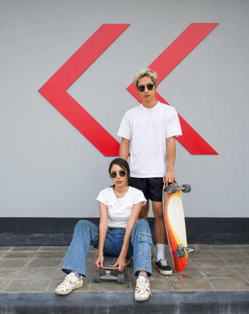 亚洲夫妇滑板后休息。一位身穿白色T恤的年轻男子手扶滑板，他的女朋友戴着太阳镜坐在前面。图片下载