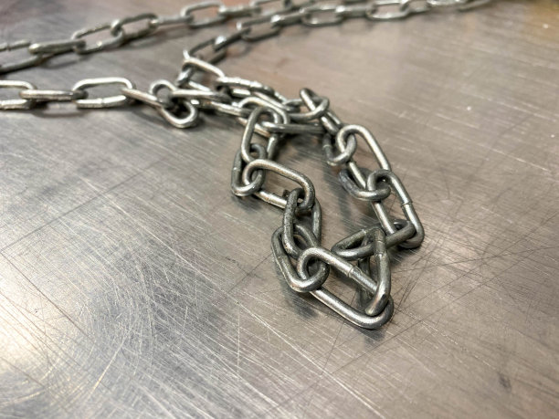 一个巨大的铁金属链，坚固有力，闪闪发光，带着链环，放在一个工业用的铁桌子上。手持锁匠工具。背景图片下载