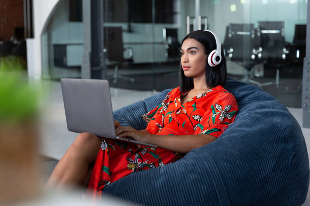 混血儿女商人的肖像坐在豆袋手提电脑戴着耳机图片下载