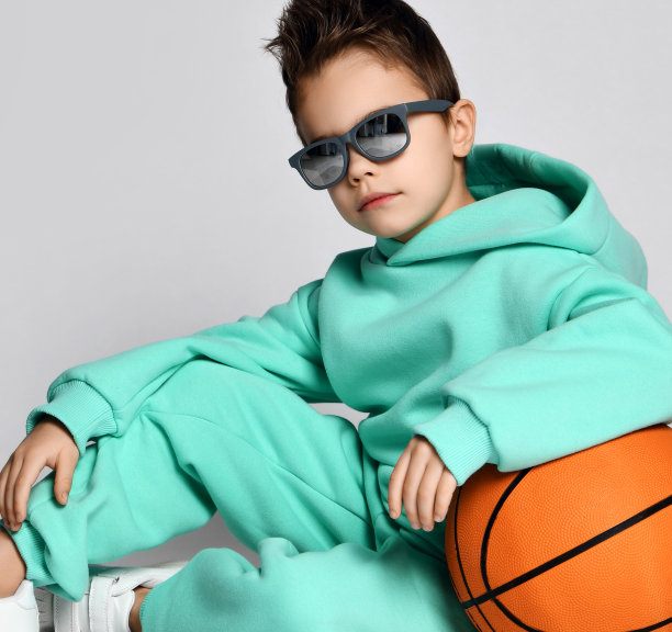 酷帅气的男孩肖像在柔和的现代绿色，薄荷色运动服帽衫和裤子坐在篮球图片下载