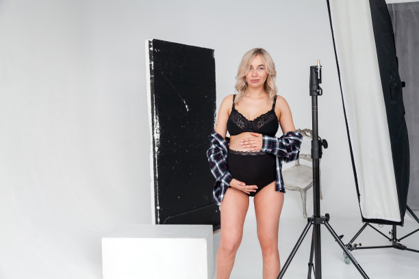 美丽的怀孕的金发女人在内衣在摄影会议与设备为高质量和美丽的照片工作室。图片下载