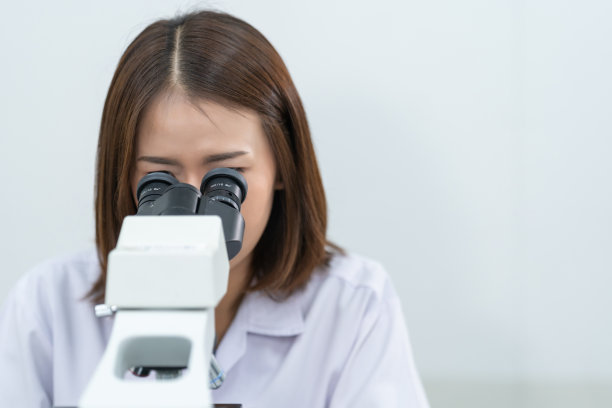 一位年轻的女科学家穿着实验服在实验室里透过显微镜做研究和实验。在实验室工作的科学家。教育库存图片图片下载