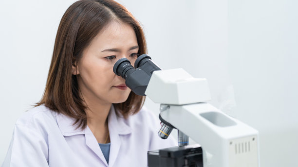 一位年轻的女科学家穿着实验服在实验室里透过显微镜做研究和实验。在实验室工作的科学家。教育库存图片图片下载