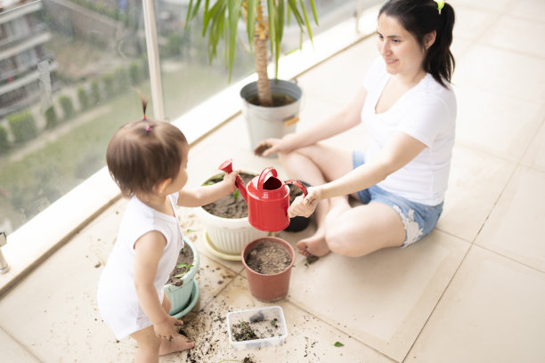 年轻的妈妈和她可爱的小女儿在自家阳台上种花图片下载