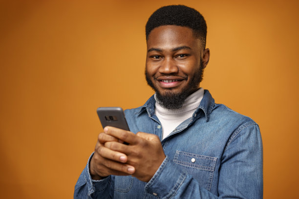一个年轻的非裔美国人在黄色背景下使用他的智能手机图片下载