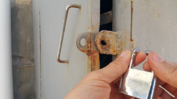 仓库老板手里拿着一把挂锁。锁是用锯子锯掉的。仓库的门开着。发现了一起入室盗窃事件。手和锁没有焦点。图片下载