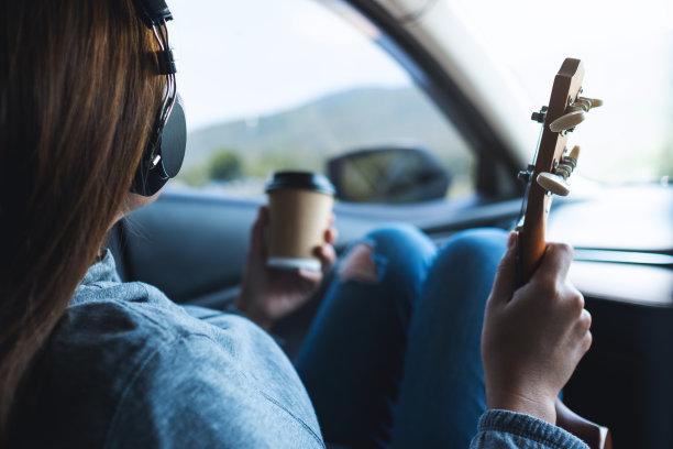 一位戴着耳机的女士在车里边听音乐边喝咖啡，手里拿着尤克里里琴图片下载