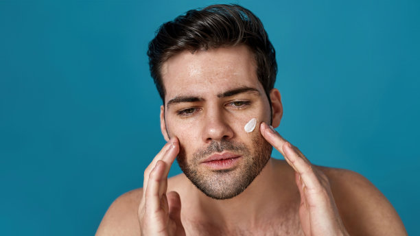 美丽的肖像，严肃的男子棕色头发，一边看一边抚摸他的脸，在皮肤上涂奶油，在蓝色的背景下孤立图片下载