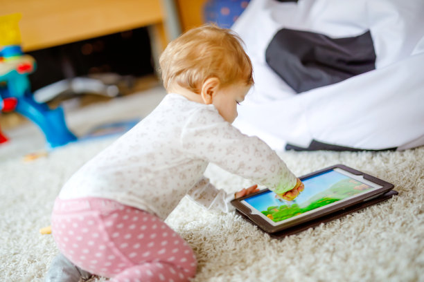 可爱可爱的小女孩在平板电脑上看动画片。蹒跚的孩子在家里触摸屏幕，在电脑上玩教育游戏。图片下载