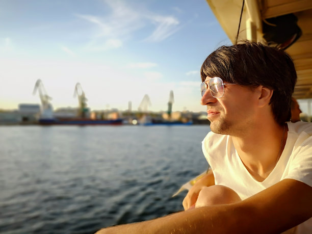 一个阳光明媚的夏日，一名年轻男子乘坐一艘观光船在第聂伯河上行驶，背景是科尔森港图片下载