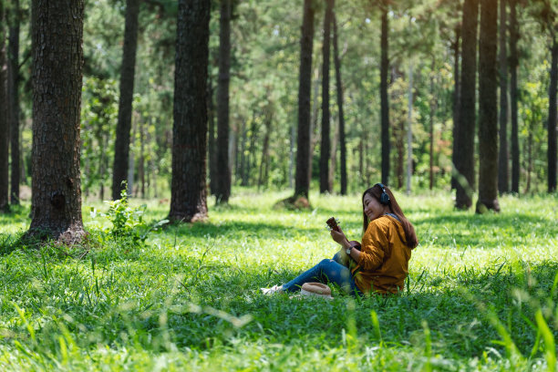 一位美丽的亚洲女子喜欢在公园里用耳机听音乐，弹奏尤克里里琴图片下载