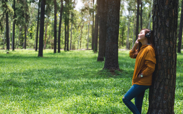一位年轻漂亮的亚洲女子喜欢在公园里戴着耳机听音乐图片下载