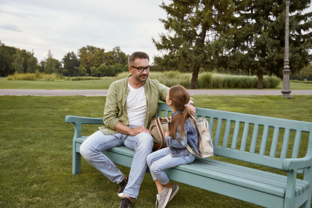 大自然中的家庭日。年轻的父亲和他可爱的小女儿坐在公园的木凳上聊天，一起在户外度过时光图片下载