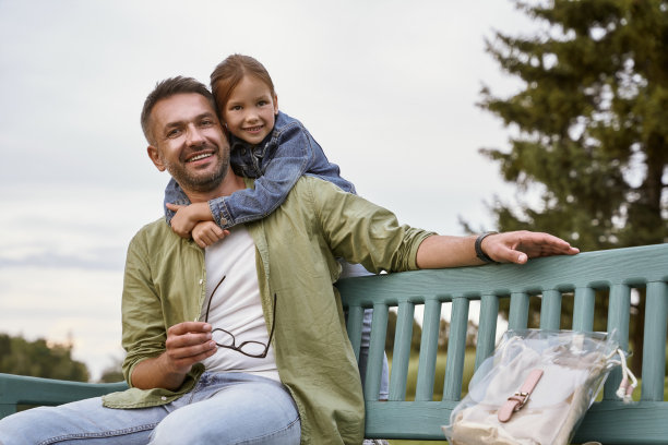 我爱我的爸爸。快乐的父亲和小女儿坐在公园的木凳上，拥抱着，看着镜头，微笑着图片下载