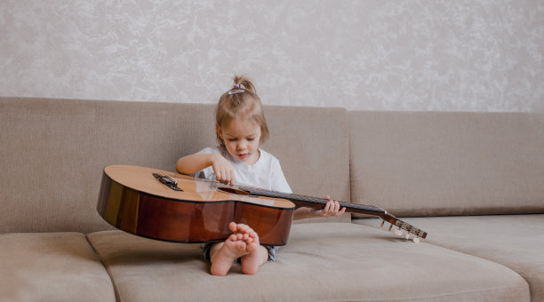 可爱的小女孩在房间的沙发上弹吉他。图片下载