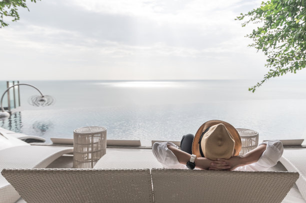 放松的假日假期，工作和生活的平衡的商人轻松愉快地休息在沙滩椅在游泳池池边海滨度假酒店与夏季海天空海景背景图片下载