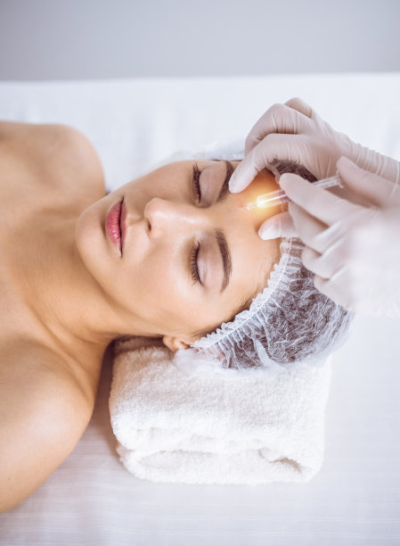 美容师做美容程序与注射器面对年轻的黑发女子在阳光水疗中心。美容药物和手术，美容注射图片下载