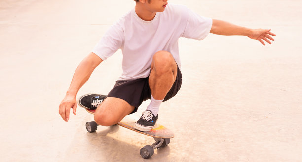 亚洲英俊的滑冰男子跪在滑板上冲浪，在白天，暑假图片下载