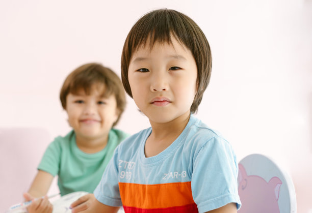 可爱的亚洲小男孩在国际幼儿园上美术课，看着相机，而他的朋友对着相机微笑。图片下载