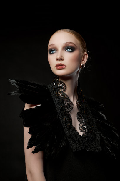 美丽的肖像年轻女子与黑色羽毛衣领周围她的脖子。女孩，在脸上画上大胆的对比妆图片下载