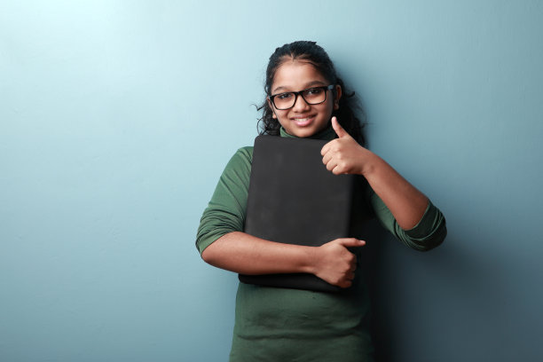 快乐的印度裔女孩拿着一台笔记本电脑，竖起大拇指图片下载