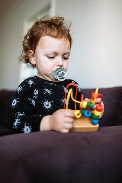 漂亮的学步儿童与奶嘴玩一个木制玩具在家里图片下载